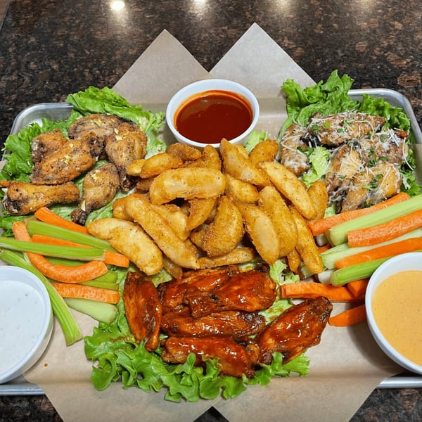 A platter of Sharon's Creole Kitchen's chicken wings, potato wedges, celery, carrots, and dipping sauces.