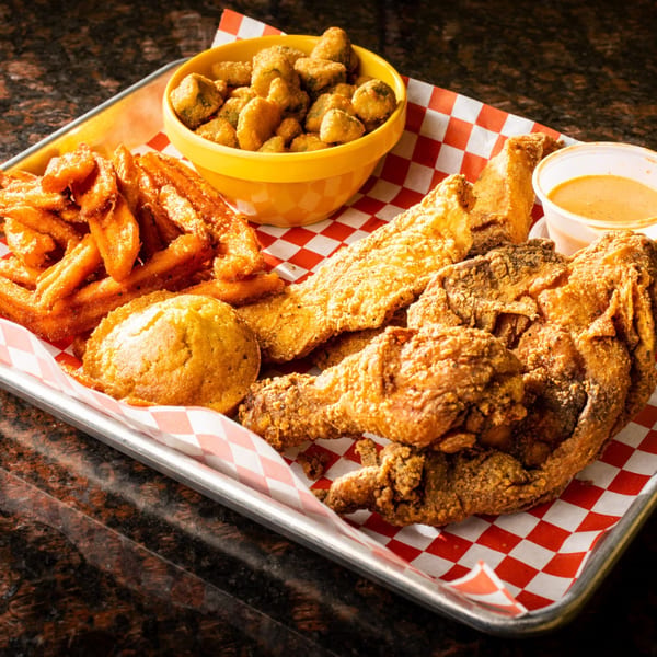 Creole fried chicken, fish, fries, hush puppies, fried okra, and dipping sauce on a tray.