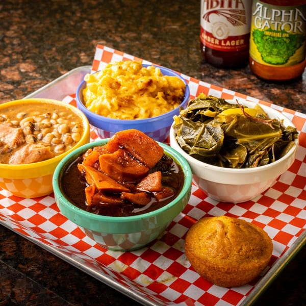 Creole side dishes: mac and cheese, collard greens, candied yams, and peas, with a cornbread muffin.