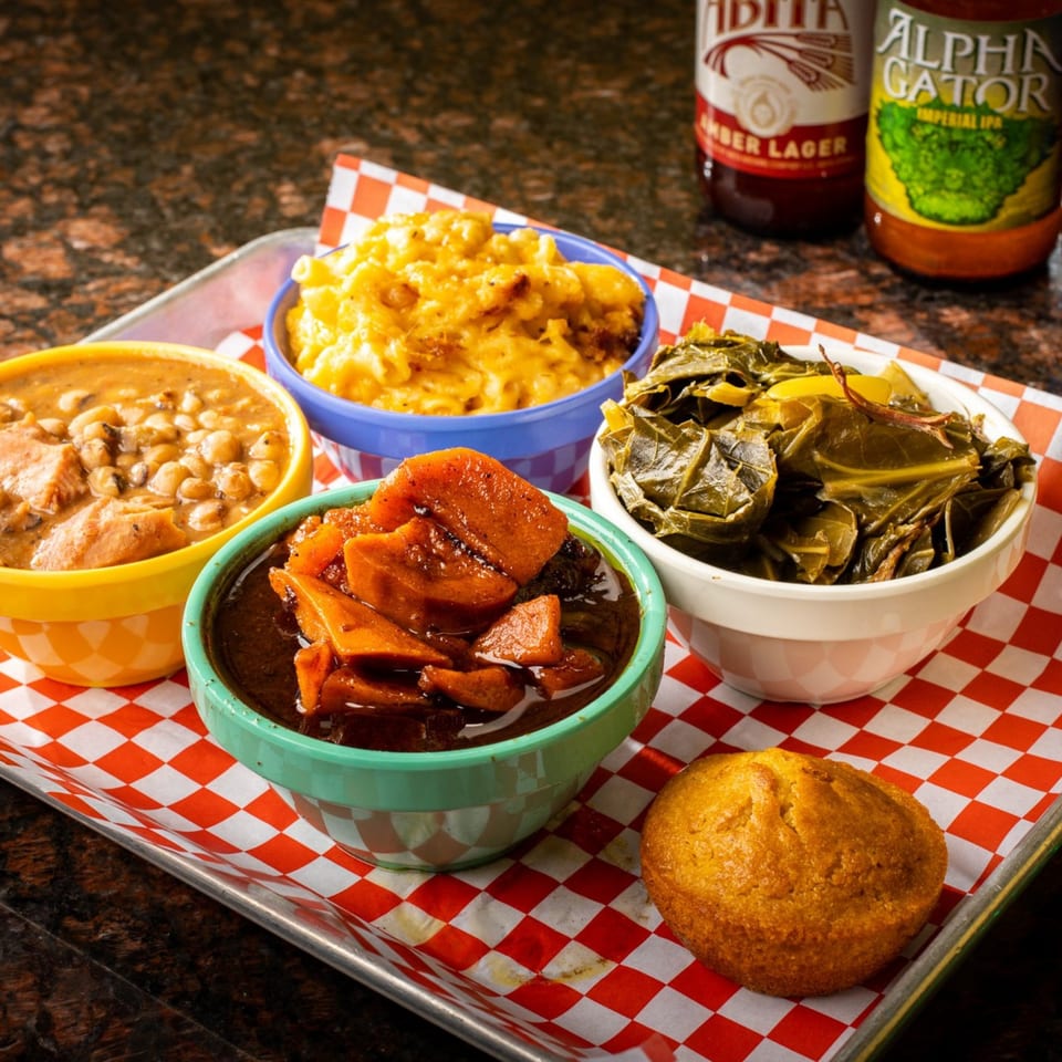 Creole side dishes: mac and cheese, collard greens, candied yams, and peas, with a cornbread muffin.