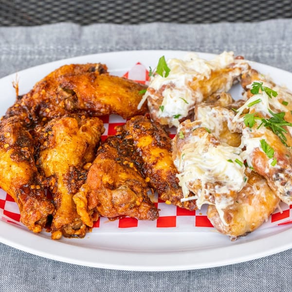 A plate of Sharon's Creole Kitchen wings, half spicy red and half creamy white, on a checkered liner.
