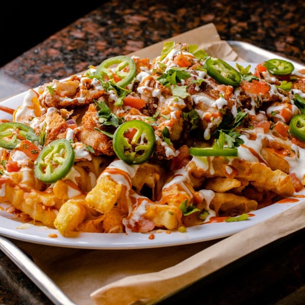 Creole kitchen's loaded fries with fried chicken, jalapenos, tomatoes, cilantro, and white sauce.